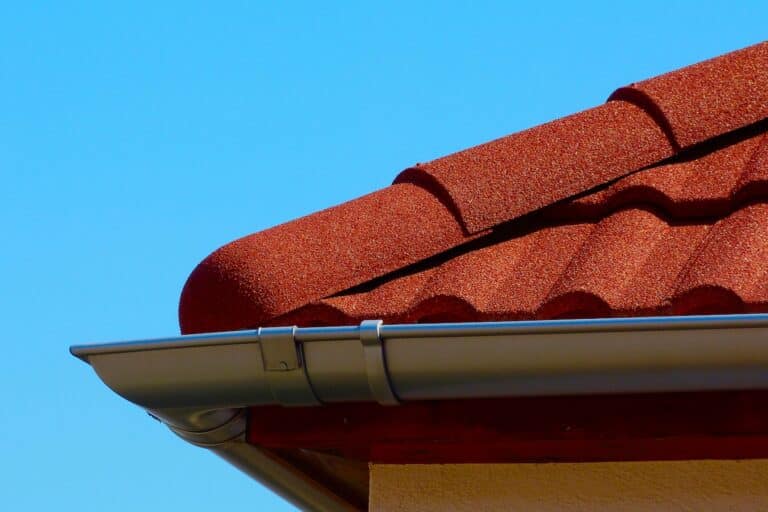 half round ridge tiles and shallow zink gutter in grey silver color. textured modern concrete tile roof. closeup detail. house construction concept. light blue sky background